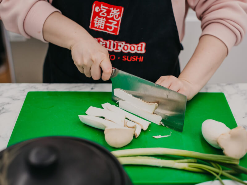 Person using a cleaver to chop matsutake mushrooms on a green cutting board